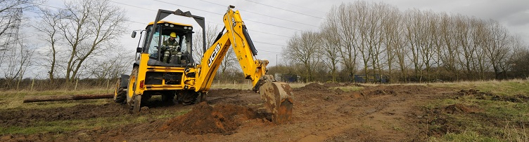 yellow J C B excavator digging in a field